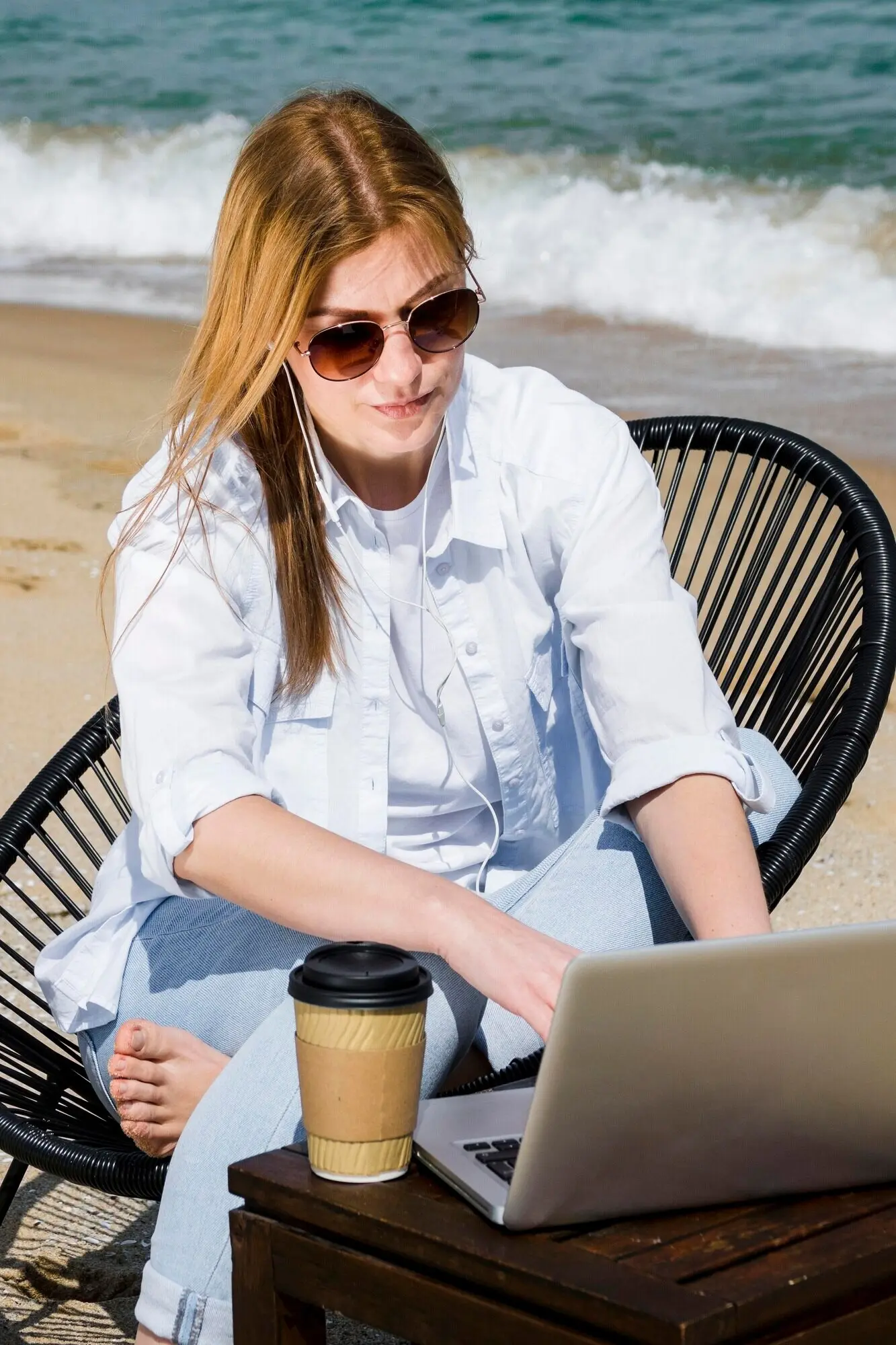 Am Strand arbeitende Frau mit Sonnenbrille und Laptop.